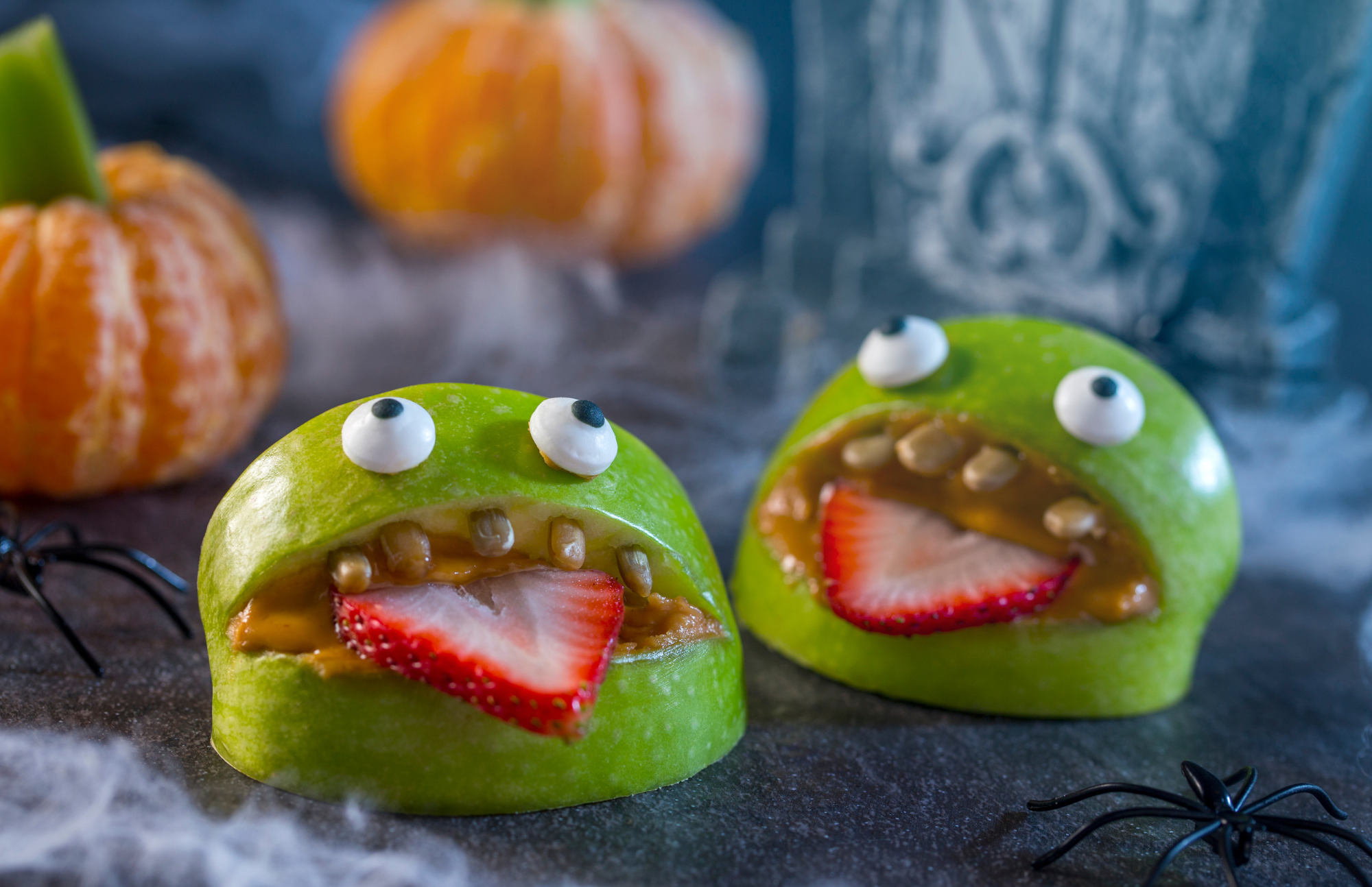 a monster face made from apples, peanut butter, strawberries, and candy eyes