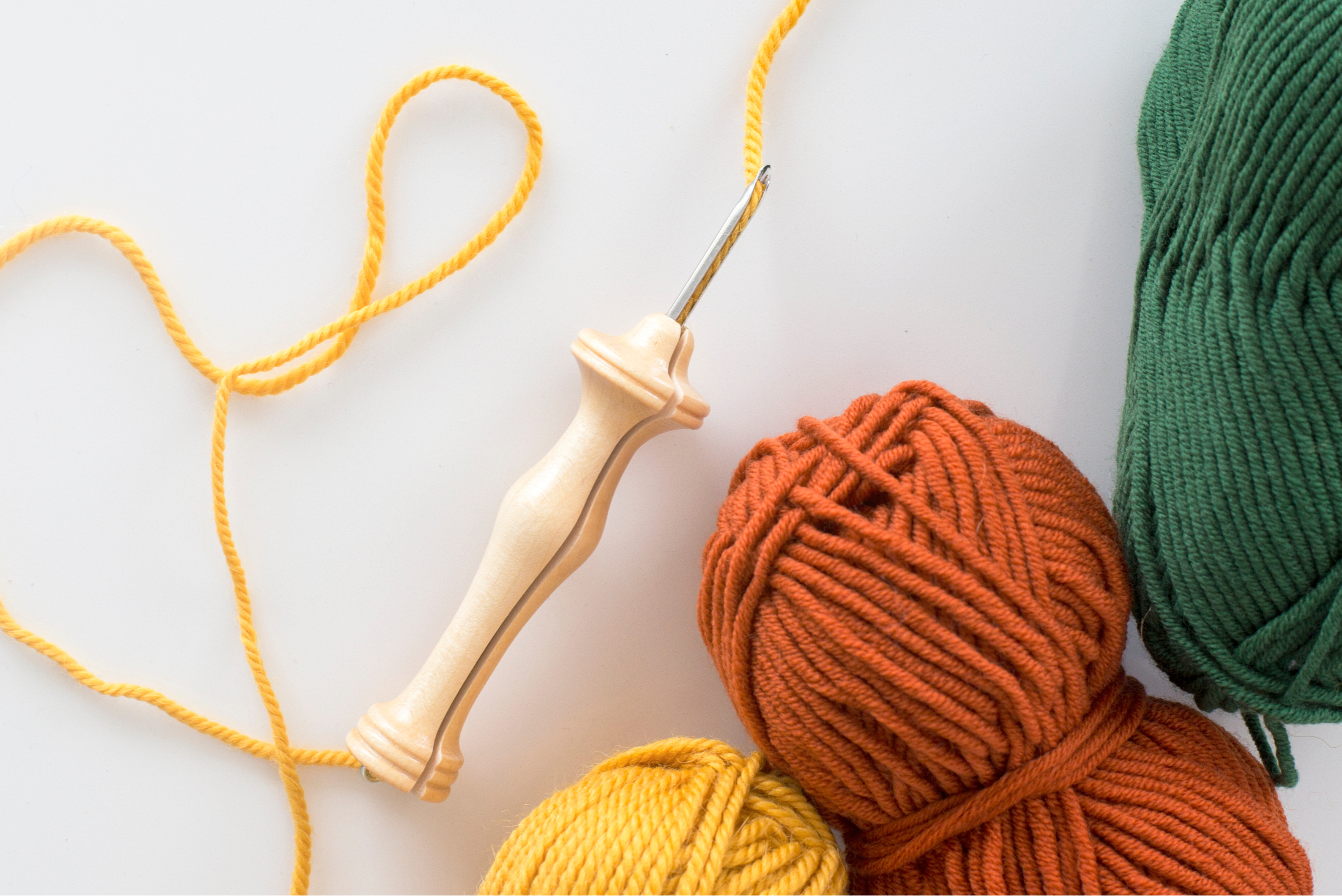 image of a punch needle tool with yellow yarn threaded through it, and skeins of orange and green yarn