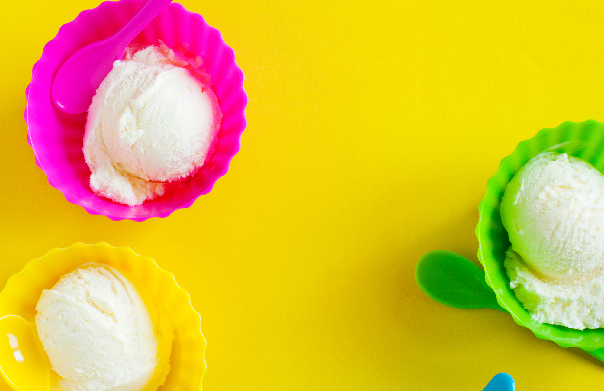 Bright yellow background, three scoops of vanilla ice cream each in bright pink, yellow, or green cups