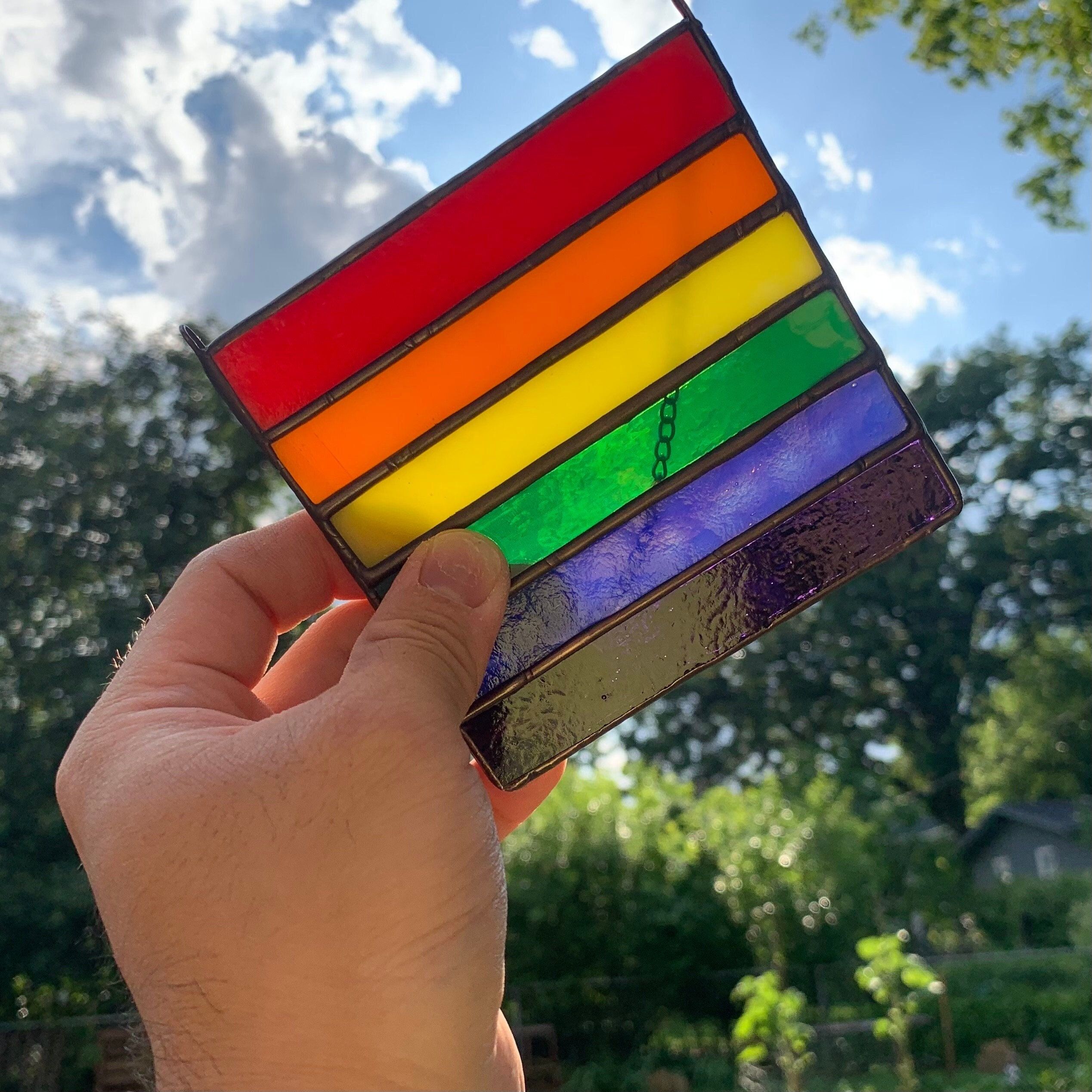 a rainbow flag suncatcher being held in the light.
