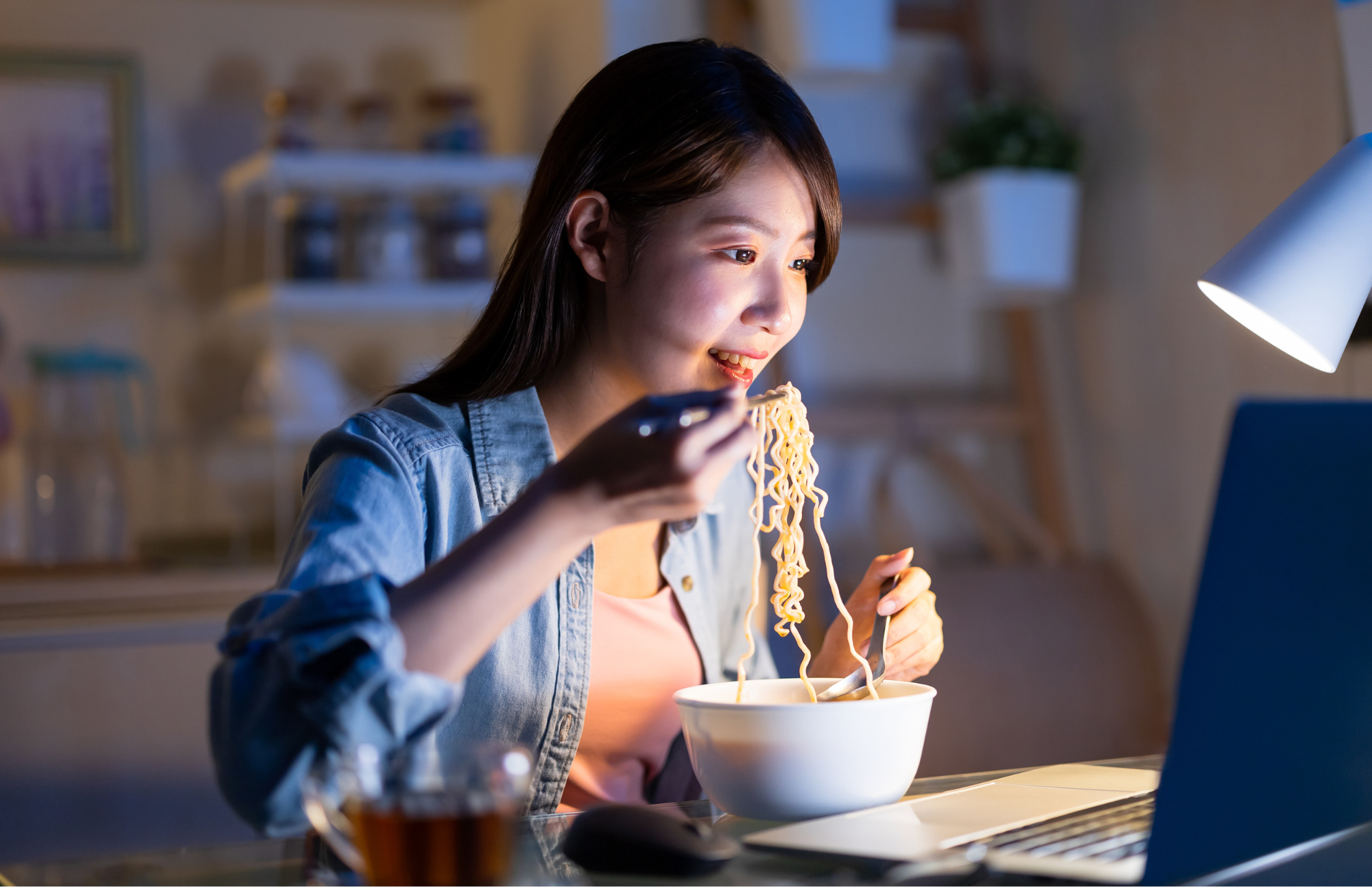 person at computer eating noodles