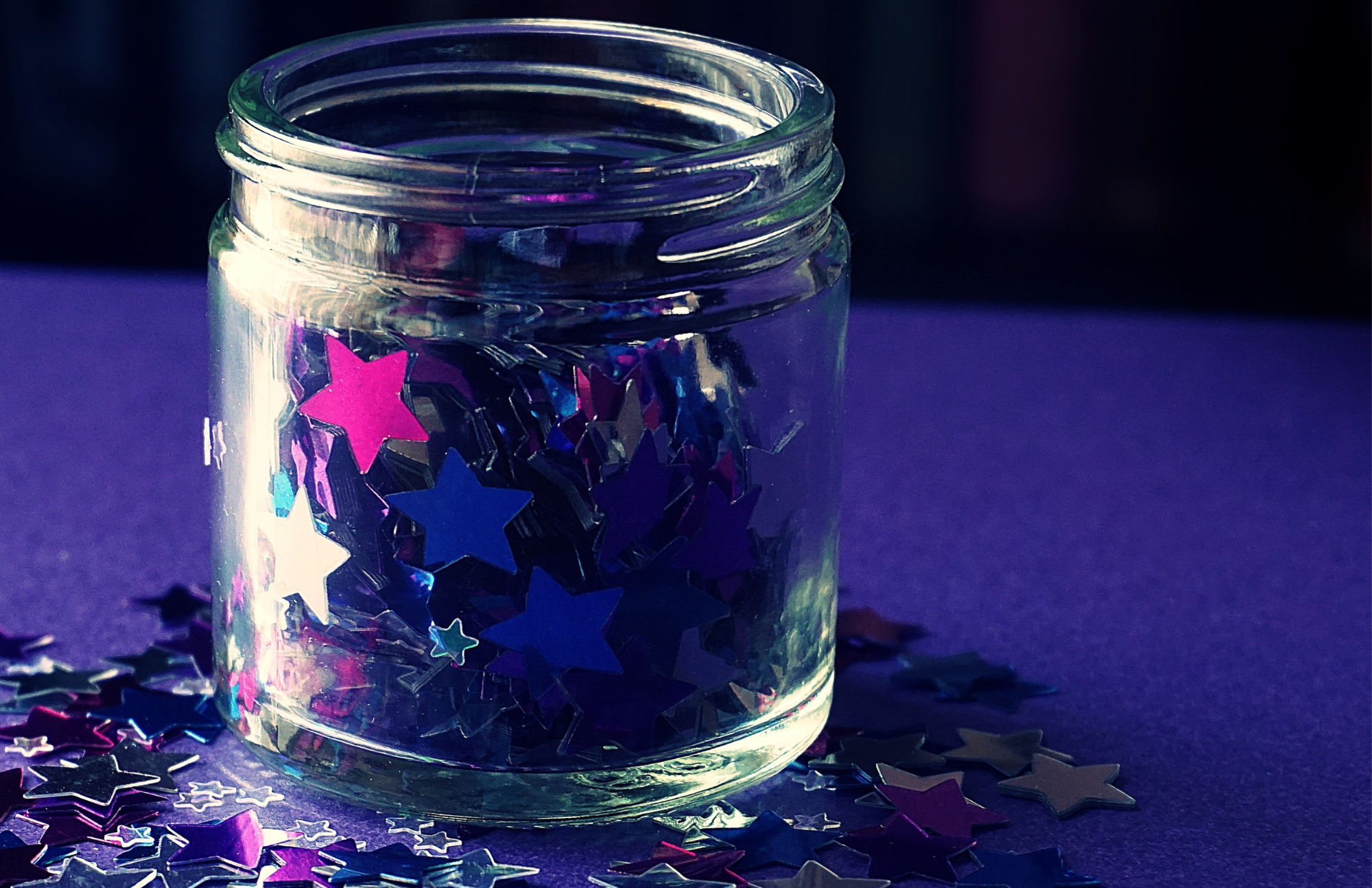 small glass jar filled with pink and purple sequin stars on a purple and black background
