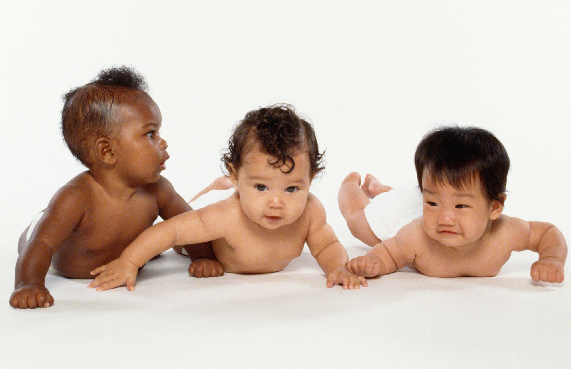 three multi racial babies on their tummies, wearing just diapers and looking completely adorable.