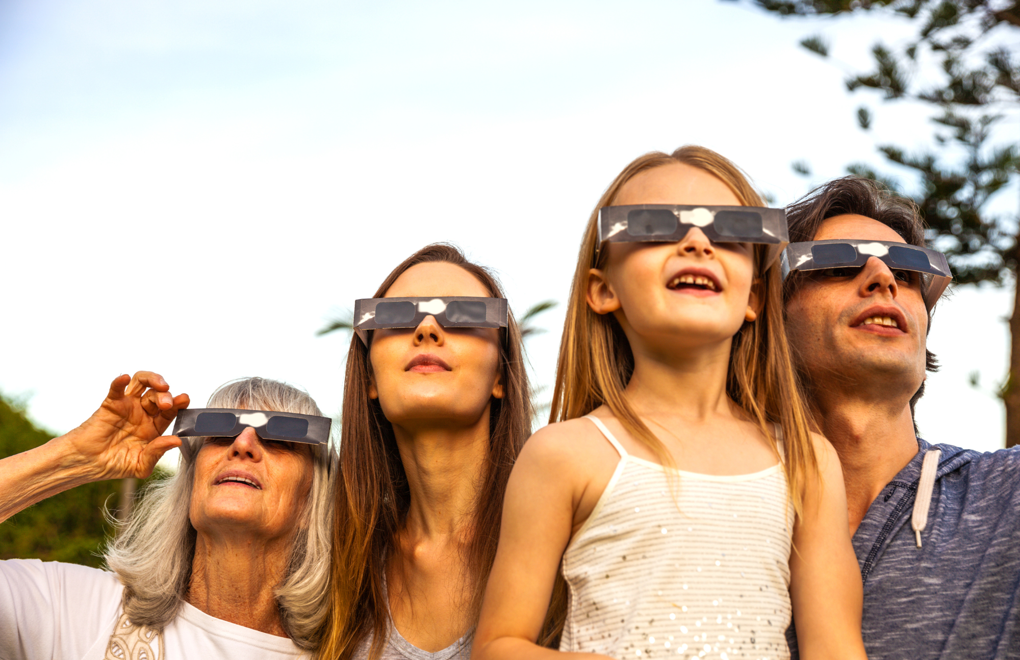 A family wearing solar eclipse glasses standing outside and looking up at the sky