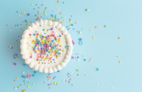 Aerial view of a round white cake with sprinkles atop a blue background