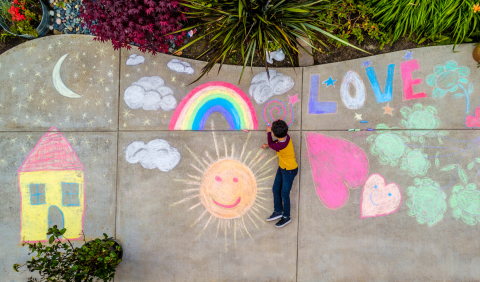 image of a child drawing on a sidewalk with chalk.