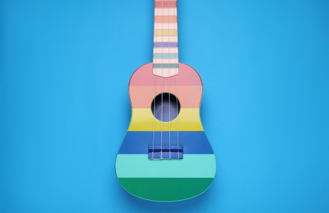 Rainbow ukulele sitting on a blank right blue background