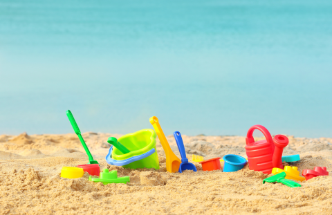 Sandy forefront with plastic beach toys, light blue water beyond