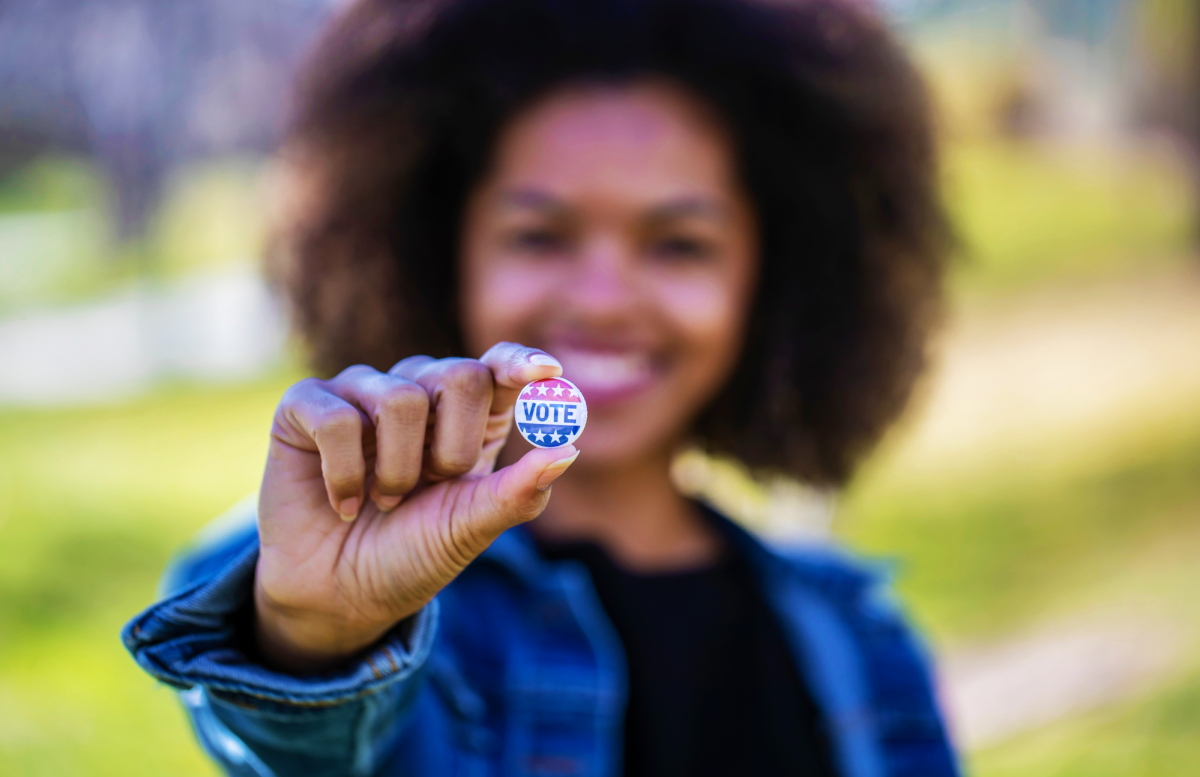 Black woman holding VOTE sticker