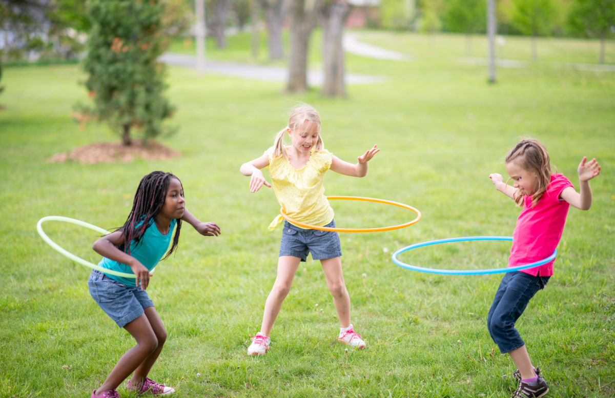 Three girls hula hooping in a grassy park