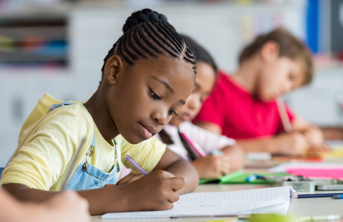 Photo of 3 kids sitting at a table and writing.