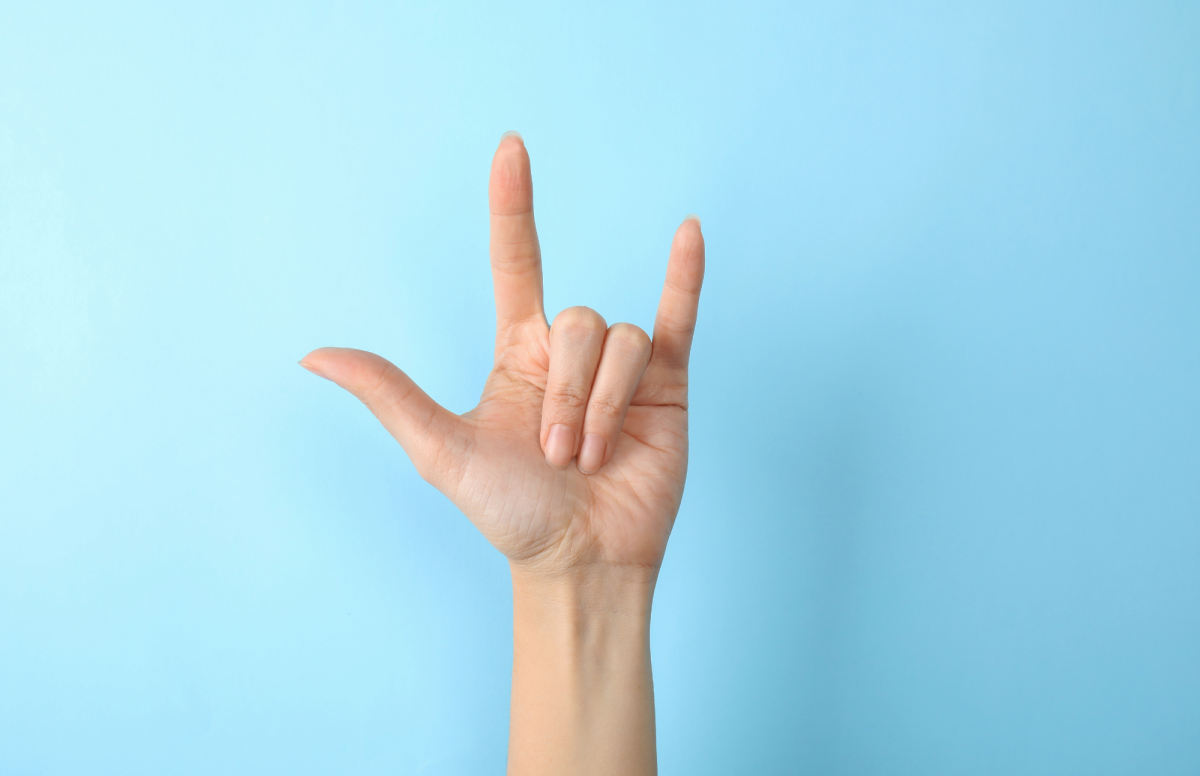 Blue background, white hand sticking straight up from bottom, doing ASL sign for I Love You.